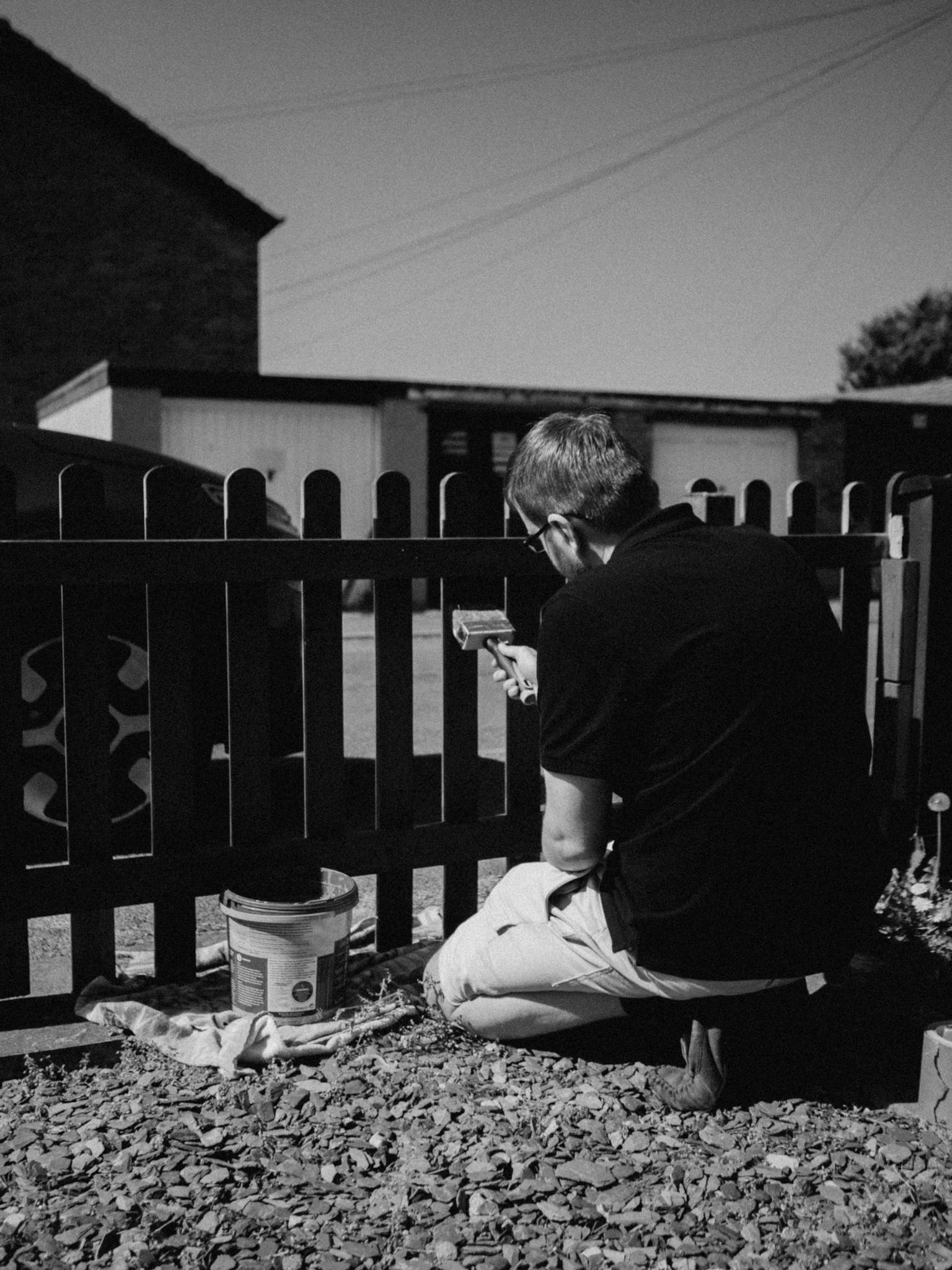 Black and white photo of a man painting a fence outdoors.